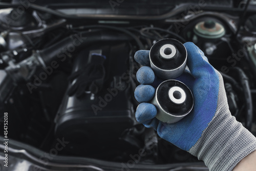 Photos master in glove holds lever silent block in his hand against background of engine