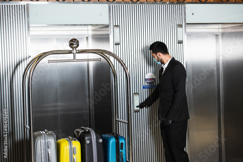 Quadro em tela bellboy in medical mask standing near bell cart near elevator in hotel