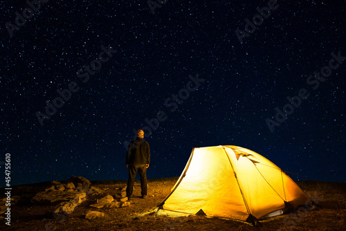 Traveler near the glowing camping tent on the background of the starry sky 