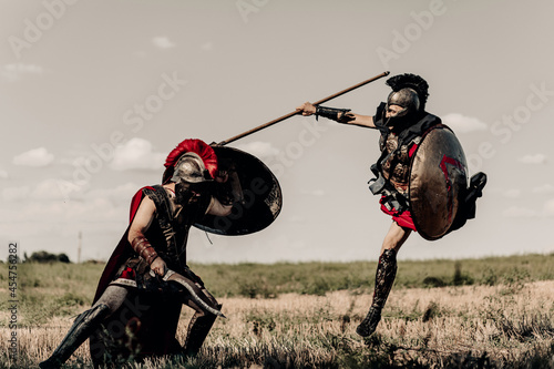 Battle with spear and sword between two ancient warriors in battle dress on meadow.