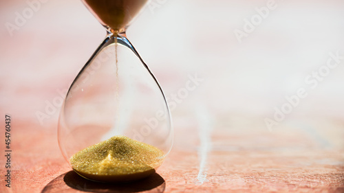 Sand running through the bulbs of an hourglass measuring the passing time in a countdown to a deadline, on a light pastel reddish background with copy space