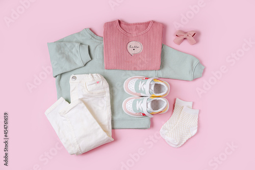 Jumpers  and pants with sneakers. Set of baby clothes and accessories for spring, autumn or summer on  pink background. Fashion kids outfit. Flat lay, top view