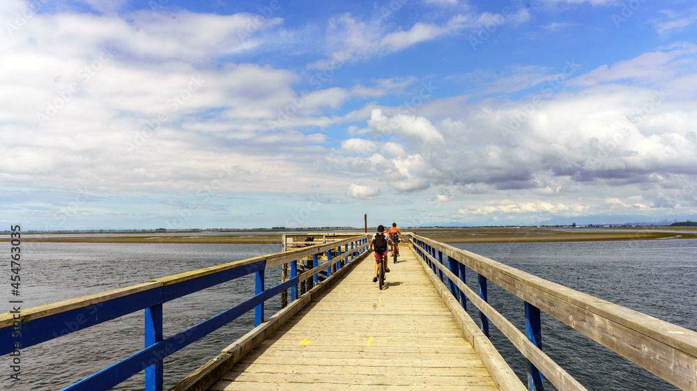 Cyclists on Blackie Spit pier at Crescent Beach, Surrey, BC, on an overcast summer day.