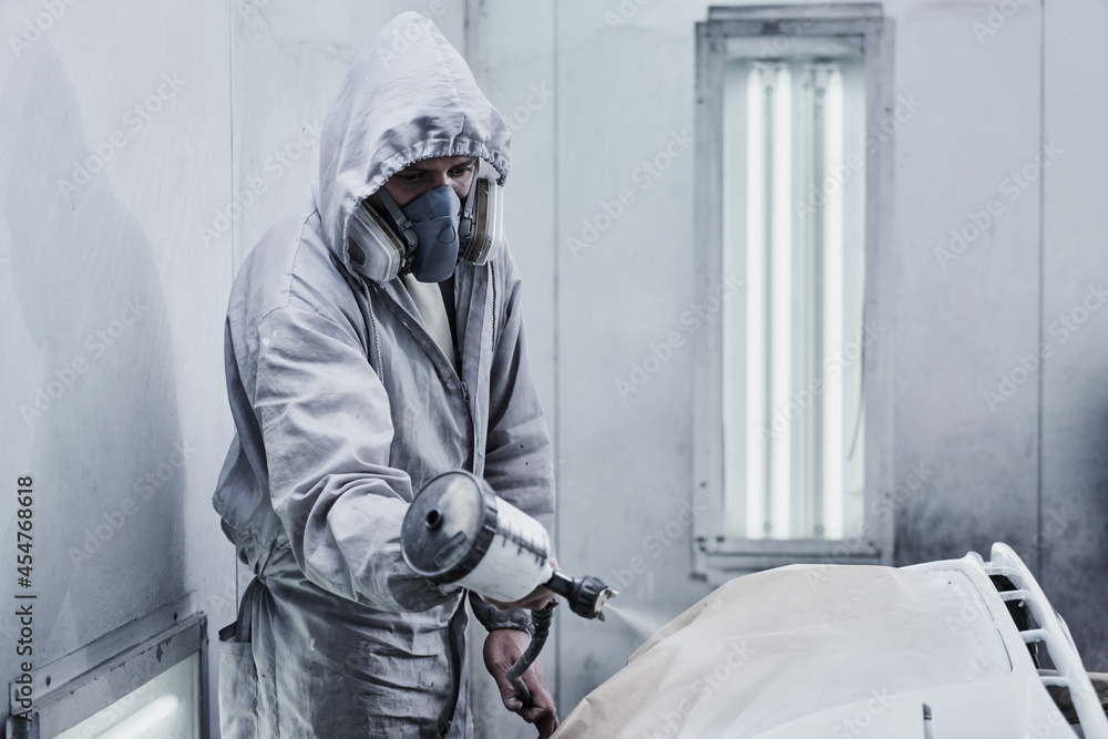 Car painting and automobile repair service. Auto mechanic in white overalls paints car with airbrush pulverizer in paint chamber. Car painting and automobile repair service. Auto mechanic in white overalls paints car with airbrush pulverizer in paint chamber.