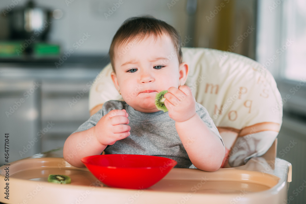 little girl on a high chair eating kiwi little girl on a high chair eating kiwi