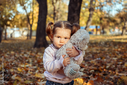 Cute toddler baby girl with soft toy playing outdoors in fall park. Little girl in the autumn park. Fall activities for toddlers.
