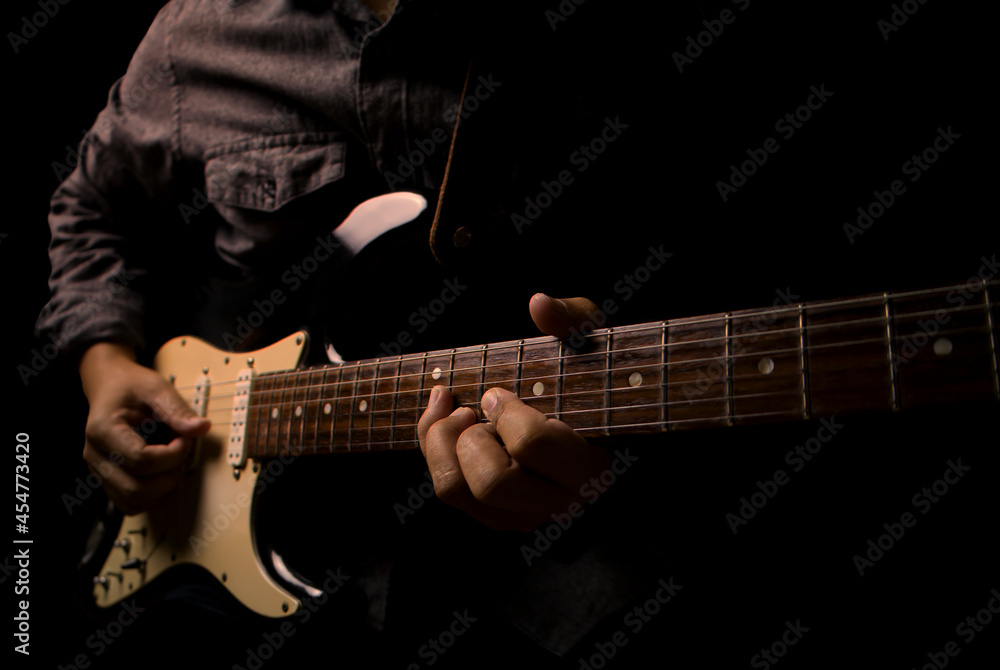 Guitarist holding electric guitar in hand and strumming chord on black background.