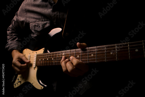 Guitarist holding electric guitar in hand and strumming chord on black background.