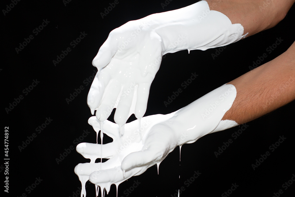 White paint flows from the fingers on a black background	