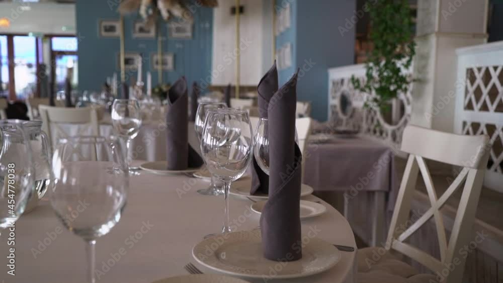 Served tables in the restaurant for celebration or dinner. Plates, glasses, gray cloth napkins. Cafe with blue walls in nautical style. Celebration dinner - wedding, birthday, party. Served tables in the restaurant for celebration or dinner. Plates, glasses, gray cloth napkins. Cafe with blue walls in nautical style. Celebration dinner - wedding, birthday, party.