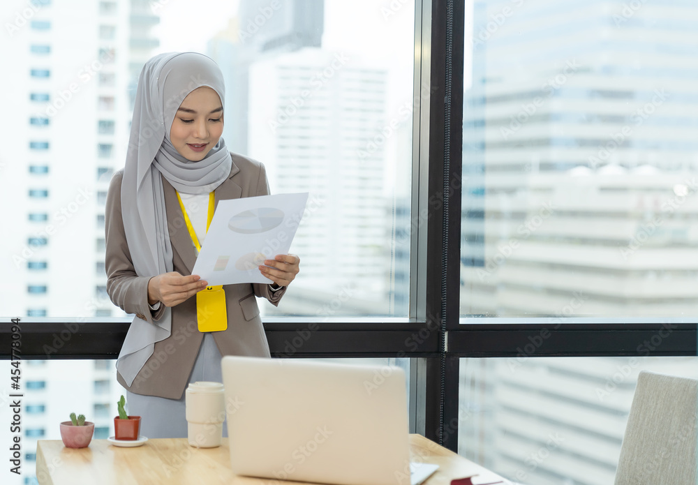 Asian Muslim businesswoman in hijab head scarf planing work with paper chart and computer laptop in the modern office Asian Muslim businesswoman in hijab head scarf planing work with paper chart and computer laptop in the modern office