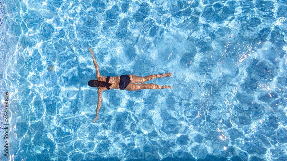 Active young girl in swimming pool aerial drone view from above, young woman swims in blue water pool, tropical vacation on holiday resort 
