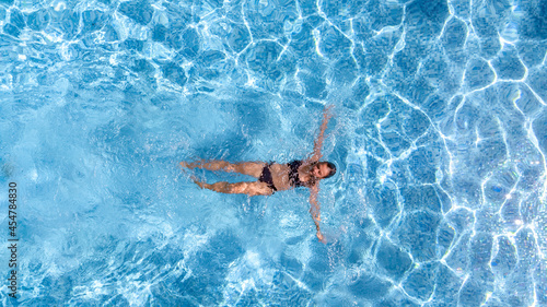 Active young girl in swimming pool aerial drone view from above, young woman swims in blue water pool, tropical vacation on holiday resort 