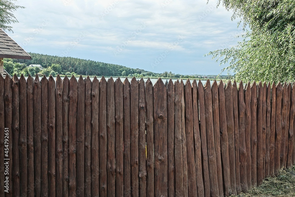 Fototapeta premium long brown wooden wall of a fence made of planks in a palisade on the street against a gray sky