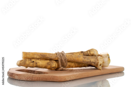 Several spicy horseradish roots on a wood board, close-up, isolated on white.