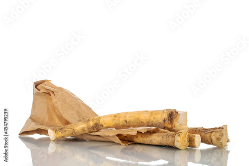 Several spicy horseradish roots with a package of paper, close-up, isolated on white.