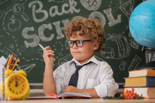 a cute curly-haired boy is sitting at a desk against the background of a blackboard with the inscription in English back to school