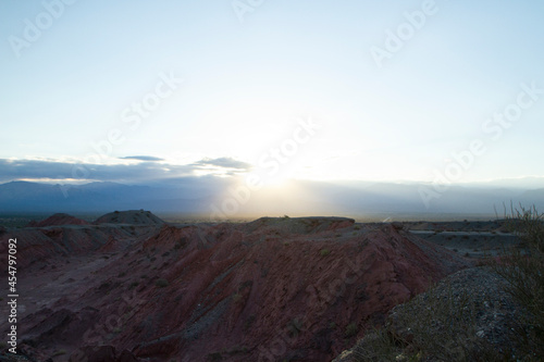 The red canyon and valley at sunset. Panorama view of the arid desert, sandstone formations, rocky mountains, lens flare and hiding sun in Talampaya national park in La Rioja, Argentina. 