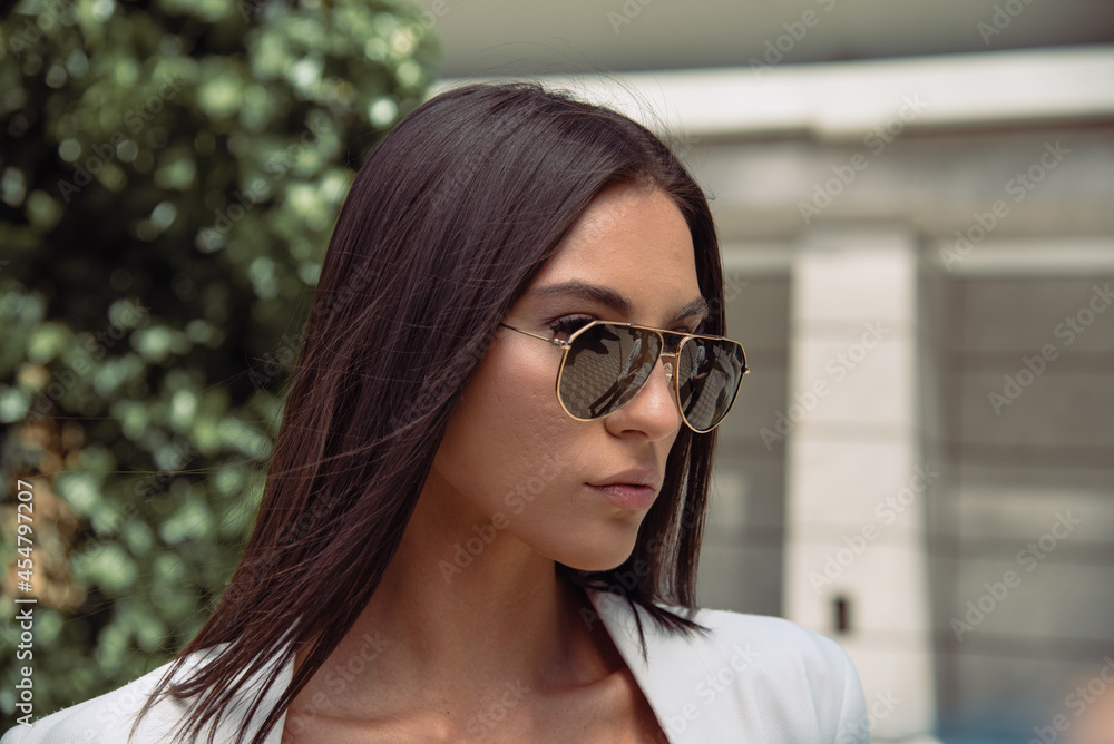 Close up image of happy brunette woman in sunglasses and summer clothes posing sideways outdoors Close up image of happy brunette woman in sunglasses and summer clothes posing sideways outdoors