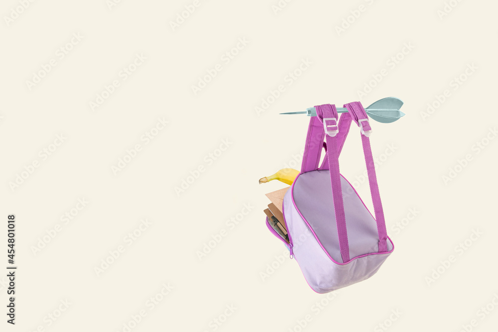 2021. Hurry up to school. Violet school backpack, flying to school on an arrow. Minimal abstract concept scene isolated on pastel yellow background. Get back to school easily and quickly. 