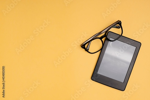 Closeup black eyeglasses and ebook reader on yellow background. Flatlay photo