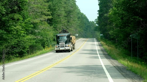 CASS CO, MN - 6 AUG 2021: Two clips of semi trailer trucks on a forest lined highway in Minnesota. Slow motion of flatbed haulers, through a windshield. photo