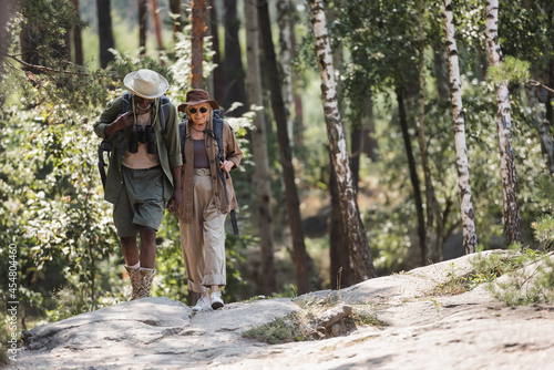 Smiling elderly woman with backpack walking near african american husband in forest. © LIGHTFIELD STUDIOS