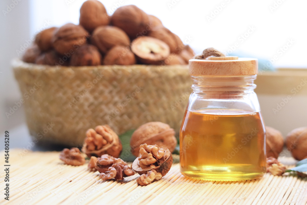 Close up of a bottle of natural cold press walnut oil with kernels and its shell in a pannier and green leaves in background. It is light-coloured and delicate in flavour and scent oil Close up of a bottle of natural cold press walnut oil with kernels and its shell in a pannier and green leaves in background. It is light-coloured and delicate in flavour and scent oil