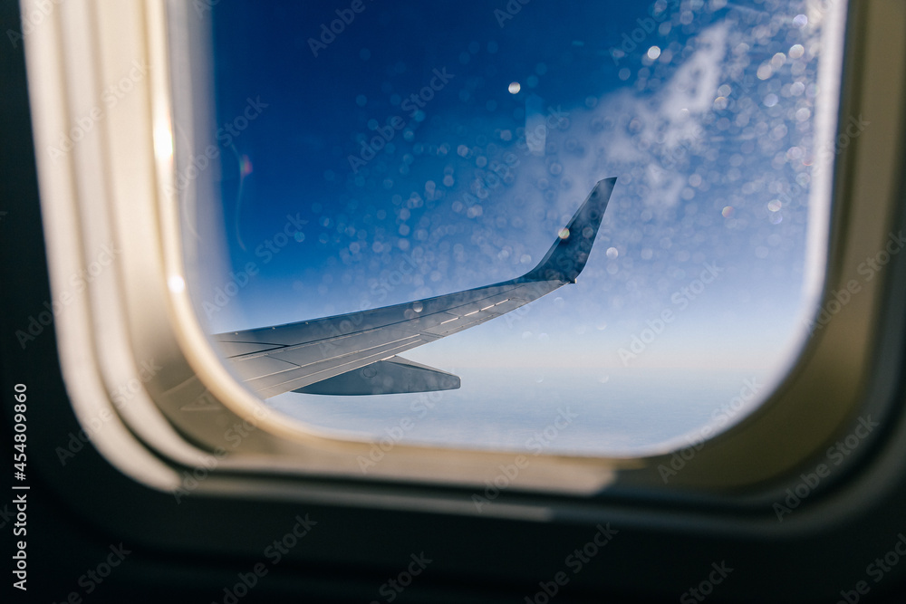 Looking out of airplane porthole. Frost on window in foreground. Focus on plane wing. Looking out of airplane porthole. Frost on window in foreground. Focus on plane wing.