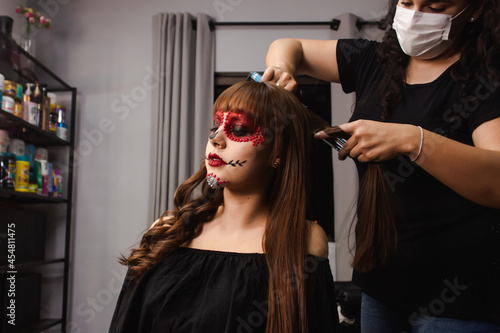 Makeup artist curling the hair of a young girl with Dia de los Muertos makeup in the beauty salon.