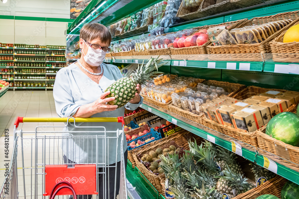 Obraz premium Grandma holds pineapples in her hand in the grocery section of the supermarket.
