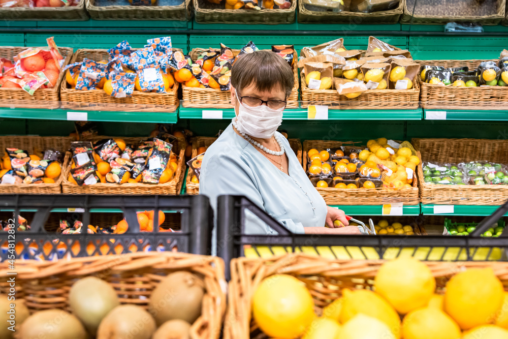 A grandmother wearing a medical mask and a shopping trolley selects products in the store.