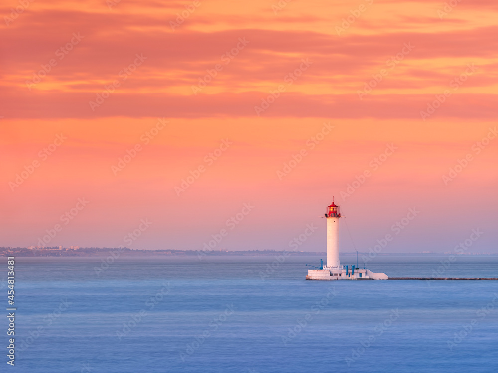View to alone lighthouse at sea under orange-pink sky in sunset time with copy space