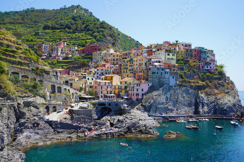 Manarola typical Italian village in the National Park of Cinque Terre with colorful multicolored buildings houses on rock cliff, fishing boats on water, Liguria, Italy