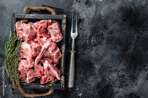 Raw diced meat with bone in a wooden tray. Black background. Top View. Copy space