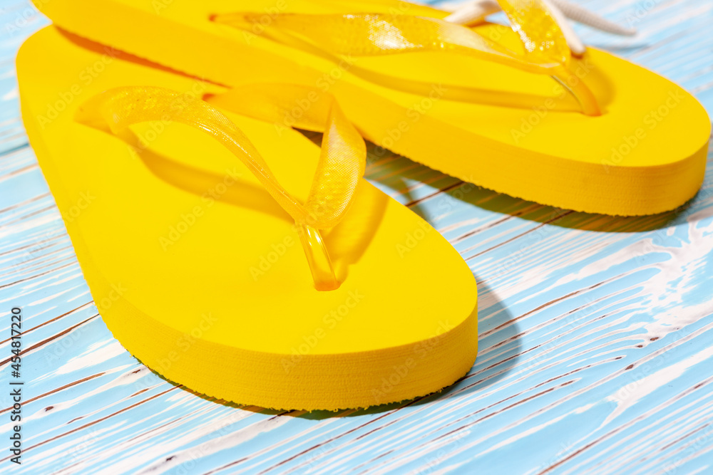 yellow rubber beach flip flops and starfish on a blue wooden background, place under the text