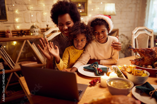 Happy black mother and kids wave during video call on Christmas day at dining table.