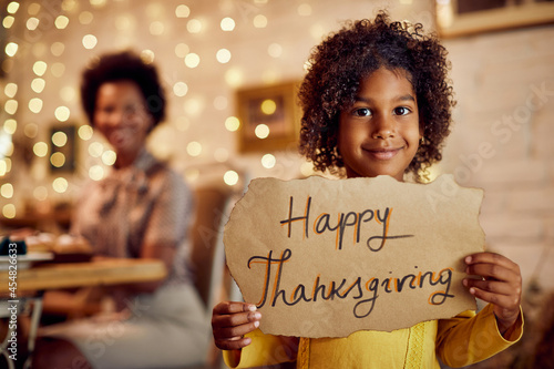 Happy African American girl holds Happy Thanksgiving sign and looking at camera.