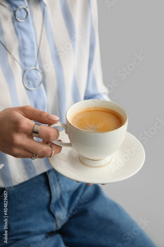 Woman drinking tasty coffee on grey background, closeup