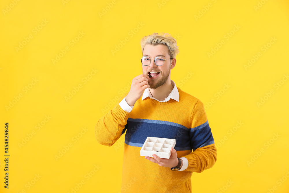 Handsome young man with box of chocolate candies on color background Handsome young man with box of chocolate candies on color background