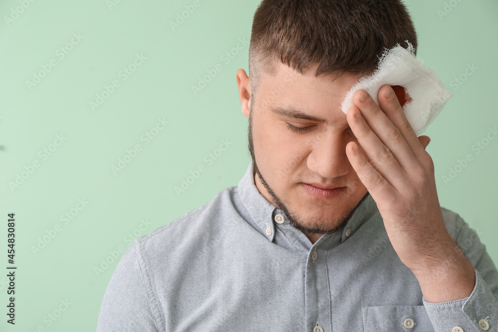 Young man applying bandage onto his forehead on color background Young man applying bandage onto his forehead on color background