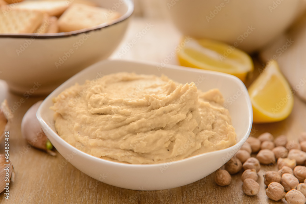 Bowl with tasty hummus on wooden background, closeup