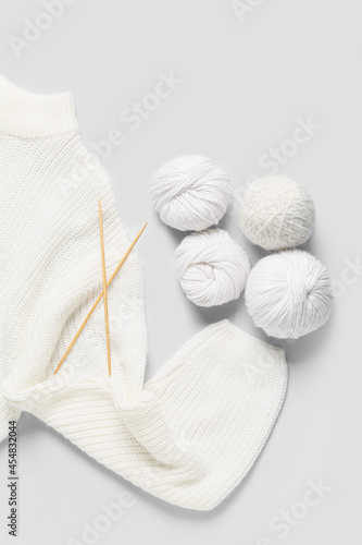 Yarn with knitting needles and sweater on white background