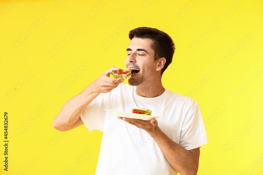 Young man eating tasty sandwich on color background Young man eating tasty sandwich on color background