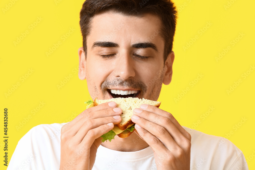 Young man eating tasty sandwich on color background Young man eating tasty sandwich on color background