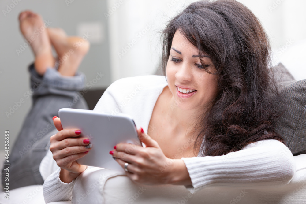 Attractive woman relaxing on a sofa reading on a tablet Attractive woman relaxing on a sofa reading on a tablet