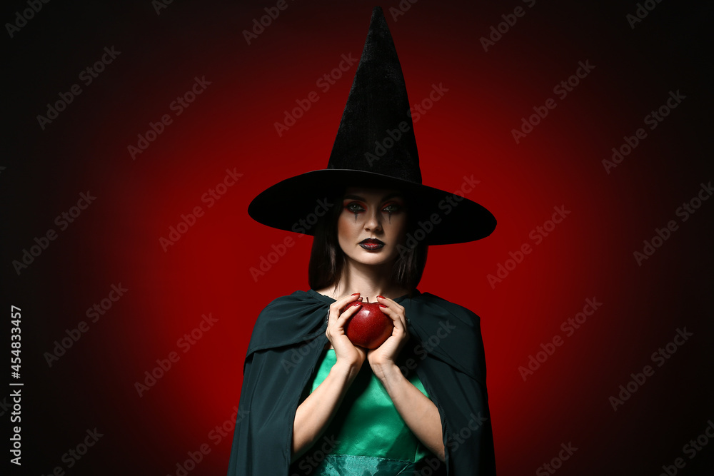 Young witch with apple on dark background