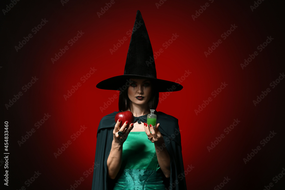 Young witch with apple and potion on dark background