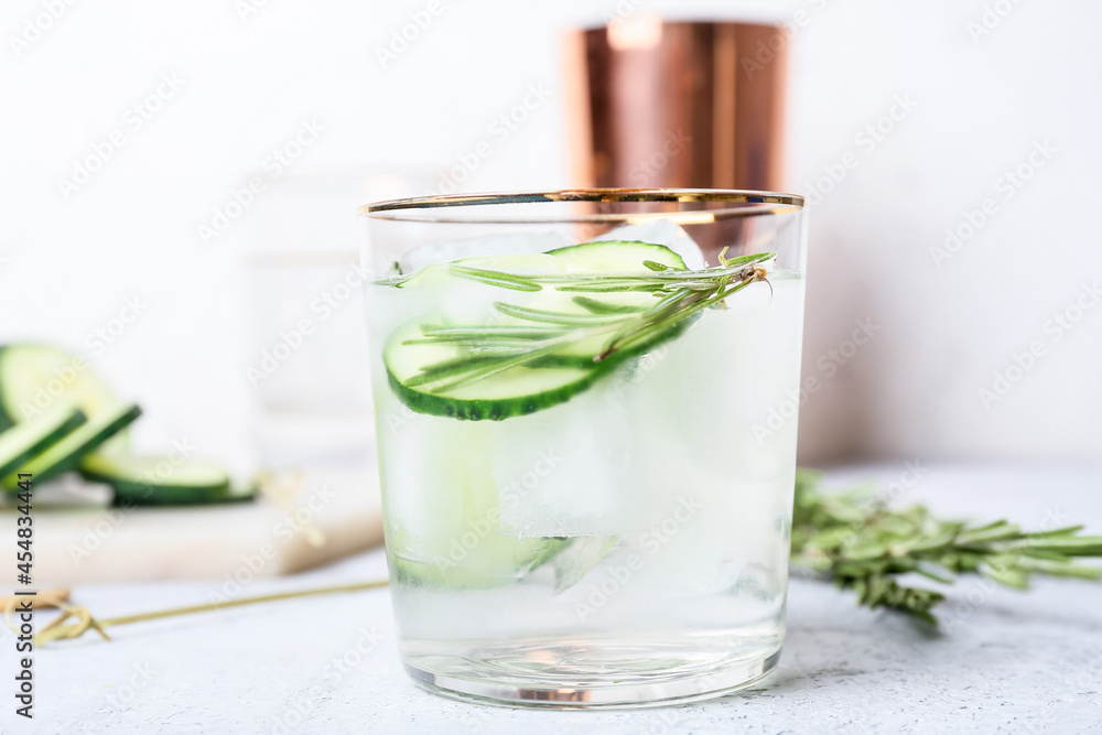 Fototapeta premium Glass of cold gin tonic and cucumber slices on light background
