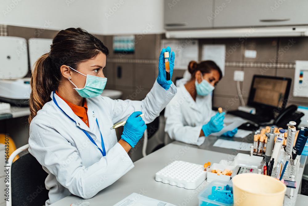 Two female scientists or technicians with face protective masks work in laboratory on human blood samples. Two female scientists or technicians with face protective masks work in laboratory on human blood samples.